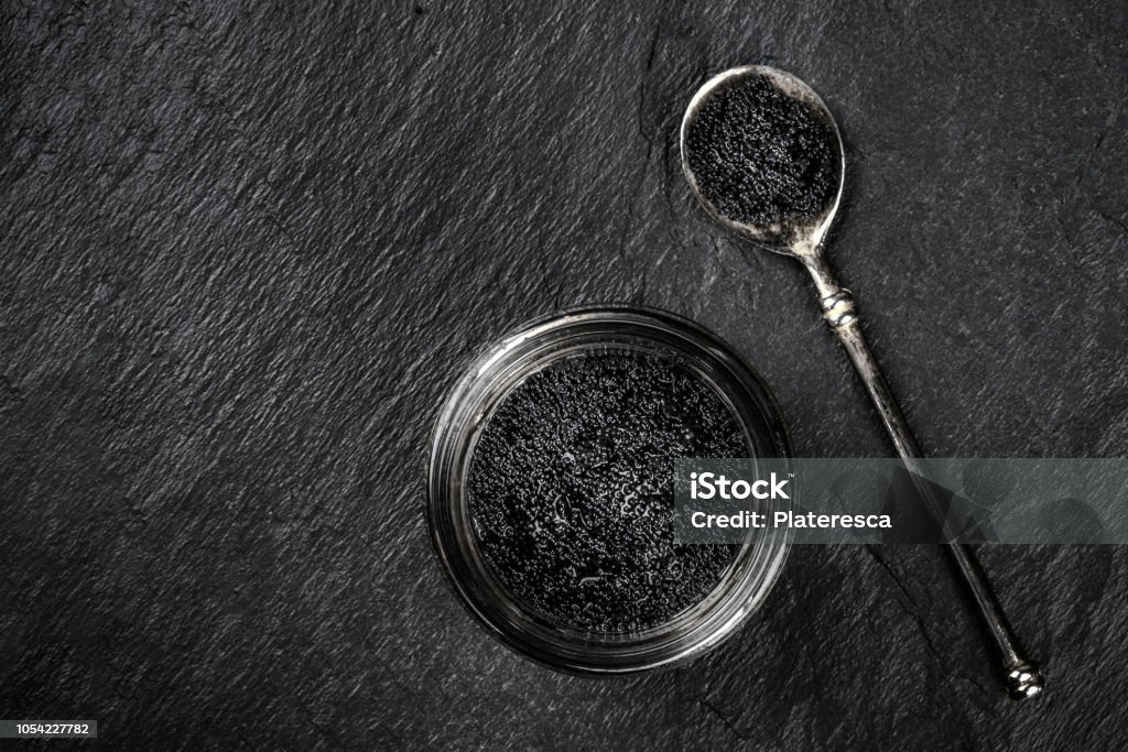 Černé rybí jikry ve sklenici a ve lžíci, zastřelené shora na černém pozadí s místem pro text - Bez autorských poplatků Břidlicí - Metamorfovaná Hornina Stock fotka Černé rybí jikry ve sklenici a ve lžíci, zastřelené shora na černém pozadí s místem pro text - Bez autorských poplatků Břidlicí - Metamorfovaná Hornina Stock fotka