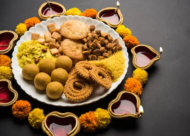 Photo of Diwali Rangoli or design made using Indian snacks/sweet and diya or lamp and flowers