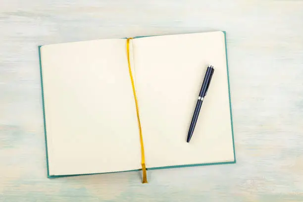 A top shot of an open journal with a pen on a light background with a place for text