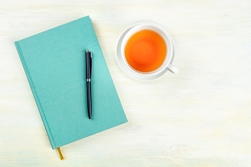 A top shot of a teal blue journal with a pen and a cup of tea, an elegant notebook on a light background with a place for text