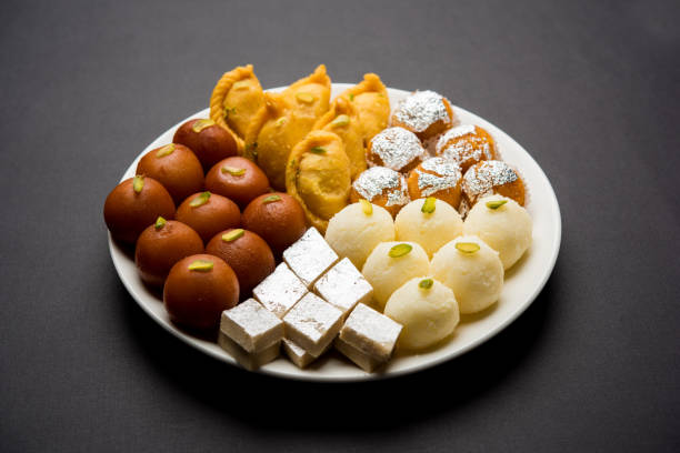 Indian sweets in a plate includes Gulab Jamun, Rasgulla, kaju katli, morichoor / Bundi Laddu, Gujiya or Karanji for diwali celebration stock photo