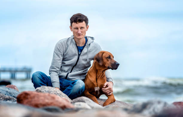 istock Man sitting on the sea shore with a dog 1054229960