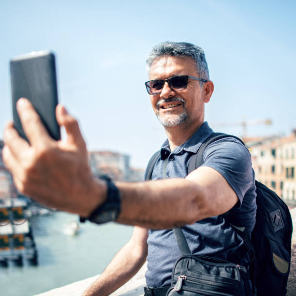 istock Senior bearded man smiling while taking selfie picture with mobile phone 1054230202