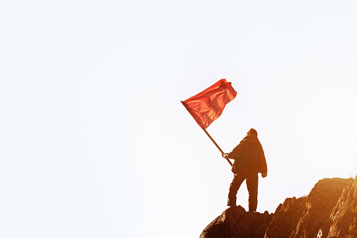 Win concept. Man with red flag stands in winner pose on mountain top. Space for text