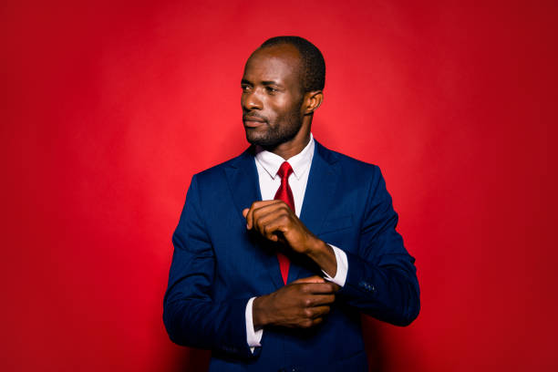Portrait of imposing elegant handsome confident success professional man in white shirt deep blue formal wear look aside fasten clasp on wrist isolated on red shine background Portrait of imposing elegant handsome confident success professional man in white shirt deep blue formal wear look aside fasten clasp on wrist isolated on red shine background man adjusting tie stock pictures, royalty-free photos & images