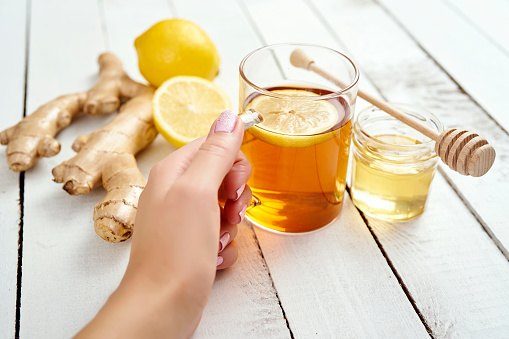 woman's hand with hot tea with lemon and honey on an wooden table with ginger pieces