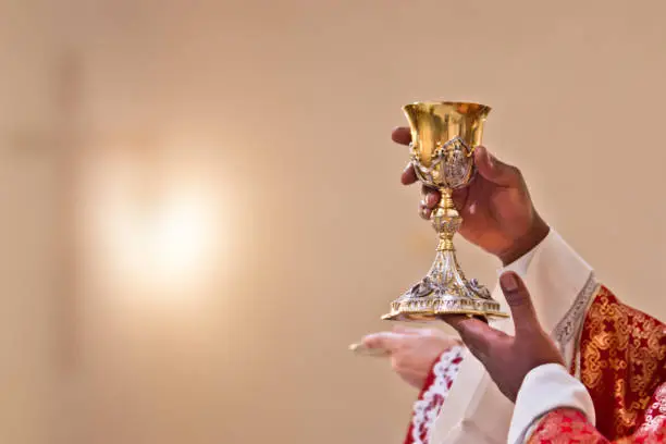 hands of the priest raise the cup containing the blood of Christ, the sacred grail