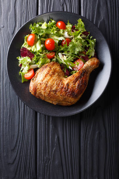 istock Fried chicken leg with fresh vegetable salad close-up on a plate. Vertical top view 1054256200