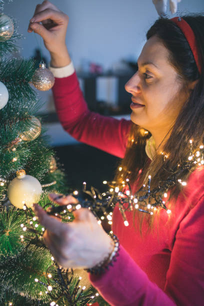 istock Happy young woman decorating Christmas tree at home 1054256682