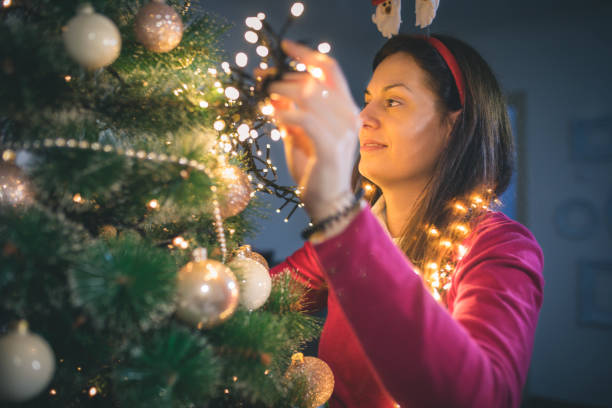 istock Happy young woman decorating Christmas tree at home 1054258384