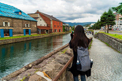 A traveller, who is a woman, is exploring and shooting a photograph of famous place, otaru canal, in japan by smartphone.