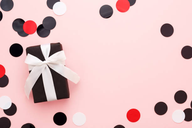 istock Gift box wrapped in black paper & white bow on pink background with space. 1054262838