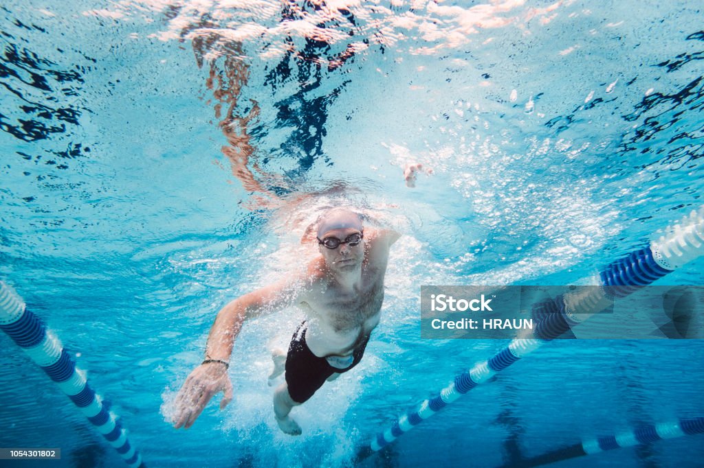 Sportsman with stoma bag swimming underwater amidst lane markers Full length of shirtless sportsman practicing freestyle swimming in pool. Mid adult male athlete is training underwater amidst lane marker. Image represents healthy lifestyle. Bag Stock Photo