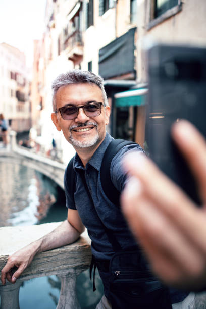 istock Senior bearded man smiling while taking selfie picture with mobile phone 1054323786