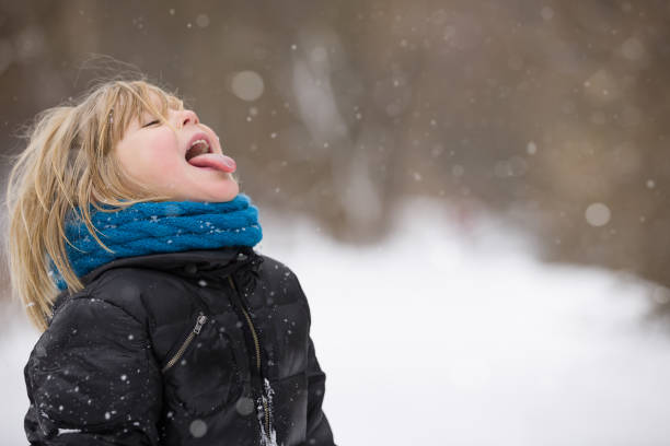 istock Cute blond kid boy catching snowflakes with his tongue. Walking in a winter park. Child having fun with snow outdoors. 1054347314