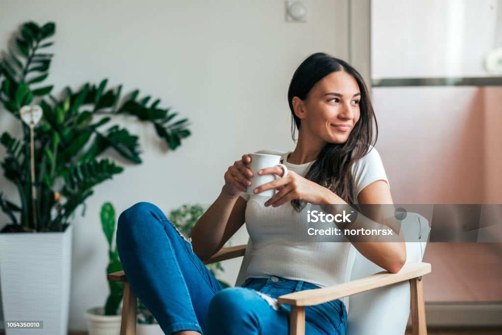 Beautiful young woman drinking tea at home. Looking away. Women Stock Photo