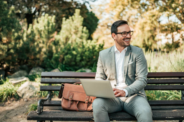 Happy young business man sitting on the bench with laptop. Happy young business man sitting on the bench with laptop. park bench photos stock pictures, royalty-free photos & images