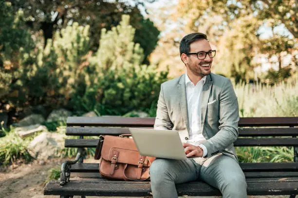 Happy young business man sitting on the bench with laptop.