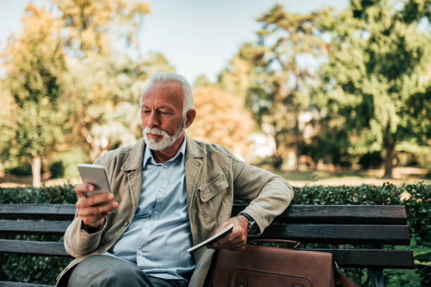 istock Senior man sitting on the bench and using smartphone. 1054350230