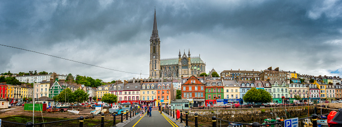 Cobh, Ireland - August 12, 2018: Central square with pier in Coph. Lot of pubs, restaurants and stores are around. In background the Cathedral of Coph. In frontz is harbor.