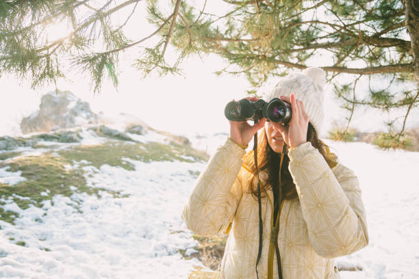 istock The girl in a White cap with a backpack in the winter in a forest looking through binoculars 1054385300