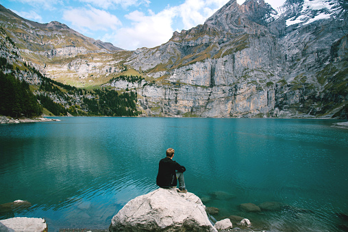 Hiker looking at view of Oeschinen Lake in the Swiss alps with beautiful turquoise water. Nature and travel concepts.