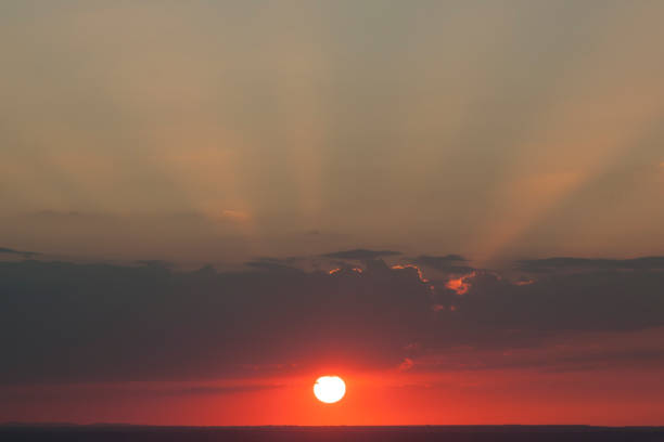 Natural sun exposure on field or meadow. Bright dramatic sky and dark earth. Countryside landscape under scenic colorful sky at sunset. Sun over the horizon. Warm colors