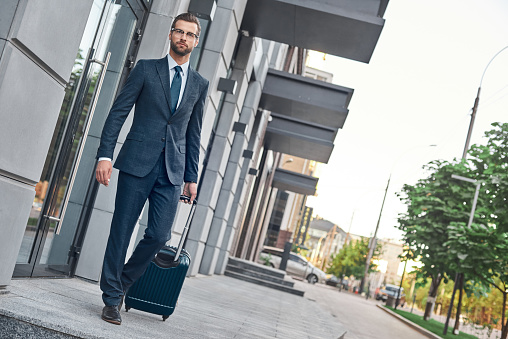 A young businessman leaves the door with suitcase, full lenght view