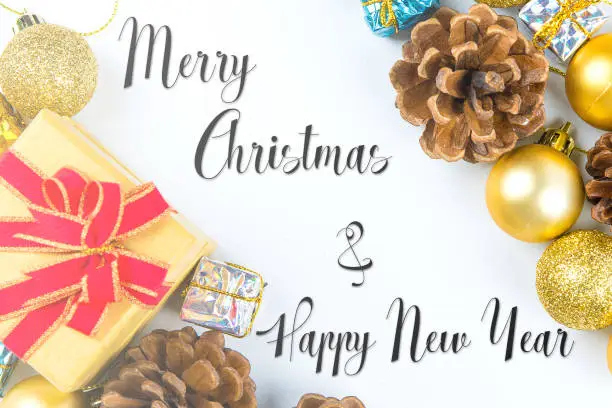 Photo of Merry Christmas and New Year typographical on white background with pine cone, gift box, golden ball and Xmas card text flatlay design.