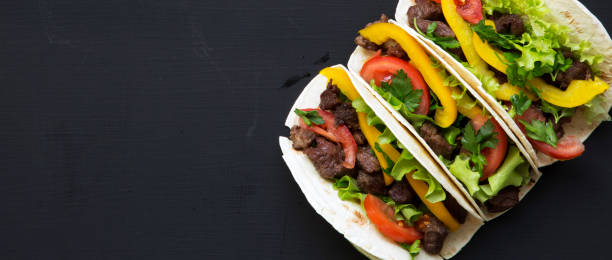istock Corn tortillas with beef and vegetables on dark background, overhead view. Mexican cuisine. Space for text. Flat lay, from above. 1054405180
