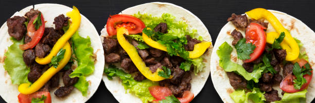 istock Corn tortillas with beef and vegetables on black background, top view. Mexican cuisine. Flat lay, from above. 1054405184