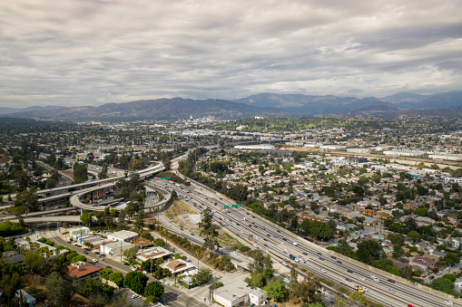 This shot is take from Echo Park neighborhood looking north with the 5 Freeway in the foreground below and the cities of Glassel Park, Cypress Park, Eagle Rock, Mount Washington, Glendal, La Canada and the Mountain range in the distance. The sky is filled with white puffly clouds.