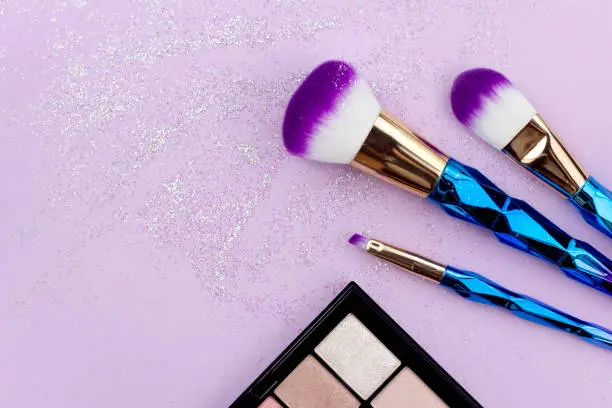 Flat lay colorful make up set with unicorn glitter on pastel purple background