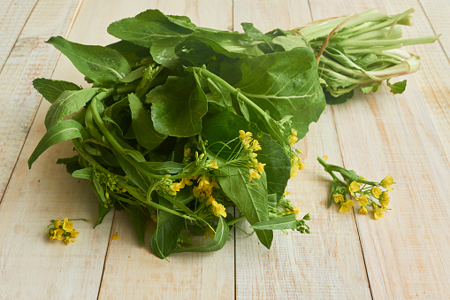 Edible mustard leaves and flowers (brassica juncea) on a wooden rustic table. The leaves and flowers of mustard are known as a very nutritious antioxidant food. Studio shot. High angle view. Close-up. Natural day lighting. Inddors photography. Horizontal composition. Copy space.