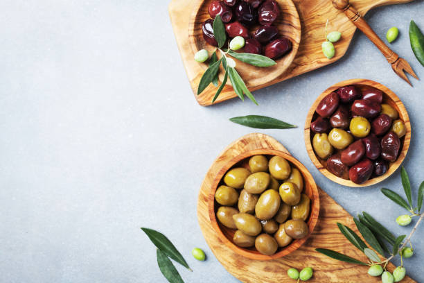 istock Marinated olives in bowls on kitchen board from olive wood top view. 1054427554