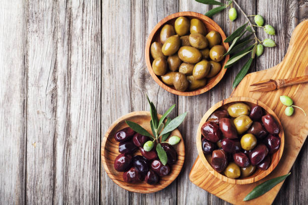 istock Pickled olives served in bowls from olive wood on rustic kitchen table top view. 1054427742