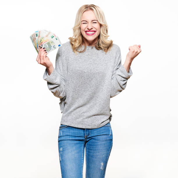 супер возбужденная молодая женщина в сером свитере и джинсах держит кучу евро банкнот, клинч кулаками, празднуя выигрышную лотерею. экстат� - women fist beautiful excitement стоковые фото и изображения