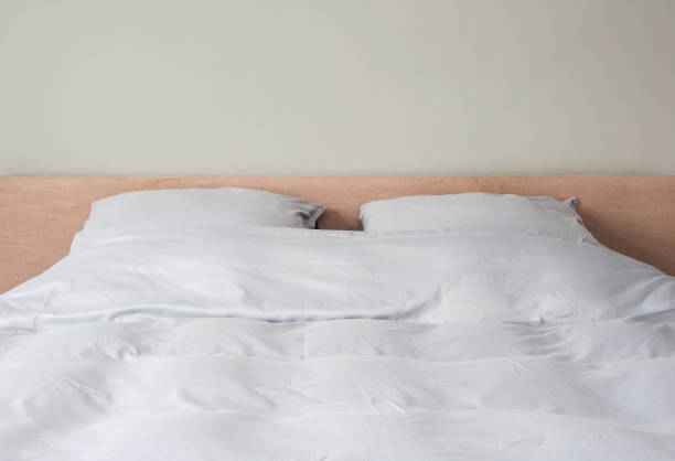 istock Bed made up with clean white pillows and bed sheets in room. Close-up. 1054470348