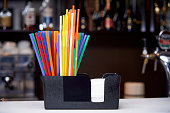 Multicolored straws with napkins stand on the bar counter.