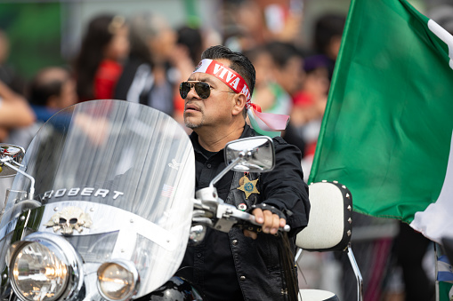 Chicago, Illinois , USA - September 9, 2018 The 26th Street Mexican Independence Parade, man riding a motorcycle, wearing a state police of illinois star and a ribbon on his head that says viva mexico and carrying a mexican flag