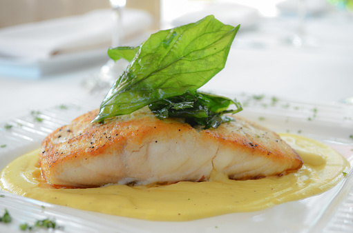 One piece of a grilled red snapper fillet with a creamy sauce, served in a white plate.