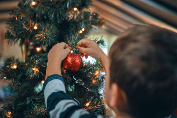 istock Little Boy Decorating Christmas Tree with Ornaments and Christmas Lights 1054612452