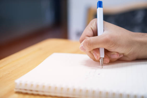 istock Man student taking and writing notes on notebook with pen in library at college university for homework. Education learning studying in school concept 1054614304