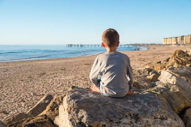 Photo of Lonely barefoot boy sitting on the rock