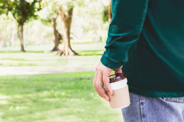 istock Man holding coffee cup or disposable cup with a black plastic cap standing in the garden green nature background. Concept happy people with leisure and drink coffee. 1054648990