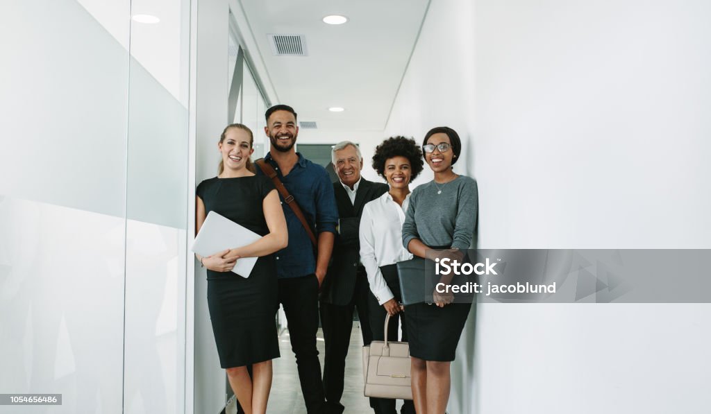 Multiracial corporate professionals in office hallway Portrait of happy business group standing together in office corridor. Multiracial business professional in office hallway. Business Person Stock Photo