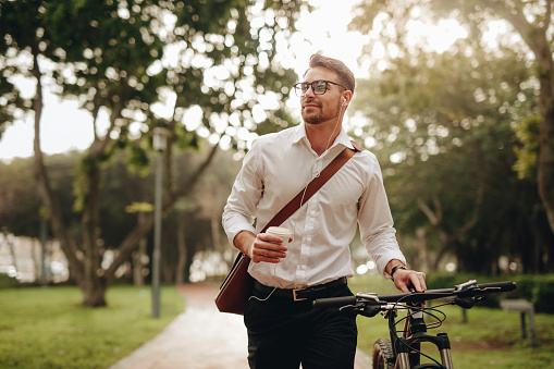 Businessman listening to music and enjoying coffee while walking to office with his bike. Man enjoying his commute to office walking with his bicycle and a coffee cup in hand.