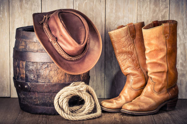 wild west retro leather cowboy hat, old boots and oak barrel. vintage style filtered photo - cowboy hat imagens e fotografias de stock