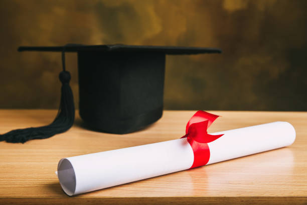 istock Graduation concept.graduation cap, hat with degree paper on wood table. 1054665004