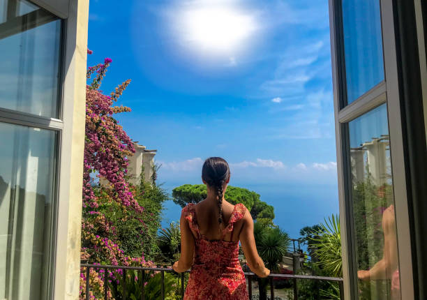 Woman at balcony against idyllic views Young woman looking out the window of her balcony against backyard, seascape and sun light. naples beach stock pictures, royalty-free photos & images